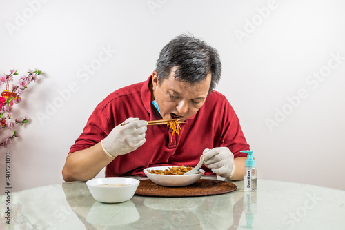 Conceptual of Asian man with face mask, glove and sanitizer dining with ample social distance space at restaurant, as part of the new normal lifestyle