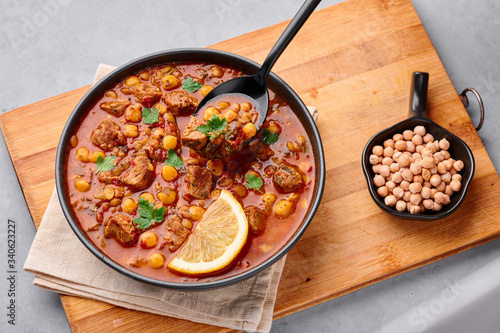 Moroccan Harira Soup in black bowl at grey concrete table top. Harira is Moroccan Cuisine dish with lamb or beef meat, chickpeas, lentils, tomatoes, ciliantro. Ramadan Iftar Food. photo