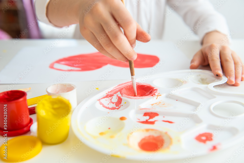 child with a brush mixes pink paint in a palette on a white table with a palette