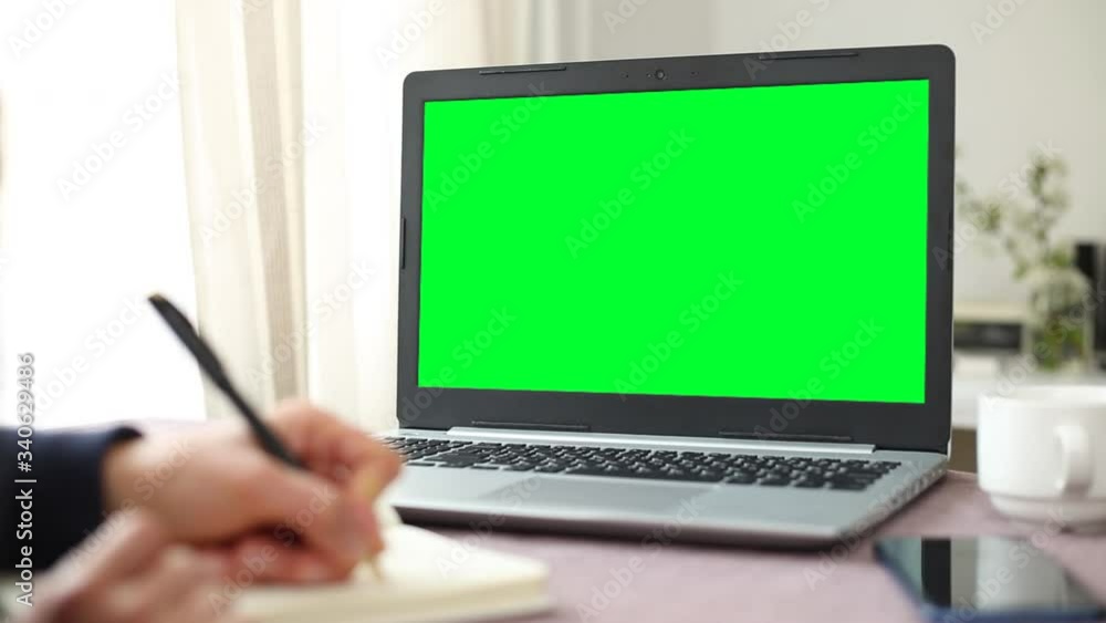 Green screen laptop monitor. Empty space, mock up. The student writes notes in a notebook. Green screen laptop monitor. Empty space, mock up. The student writes notes in a notebook.