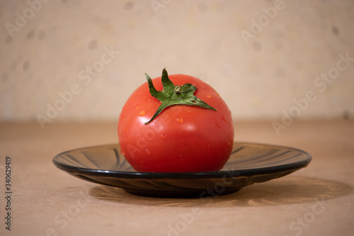 composition of a red tomato, round shape on a black saucer, still life.
