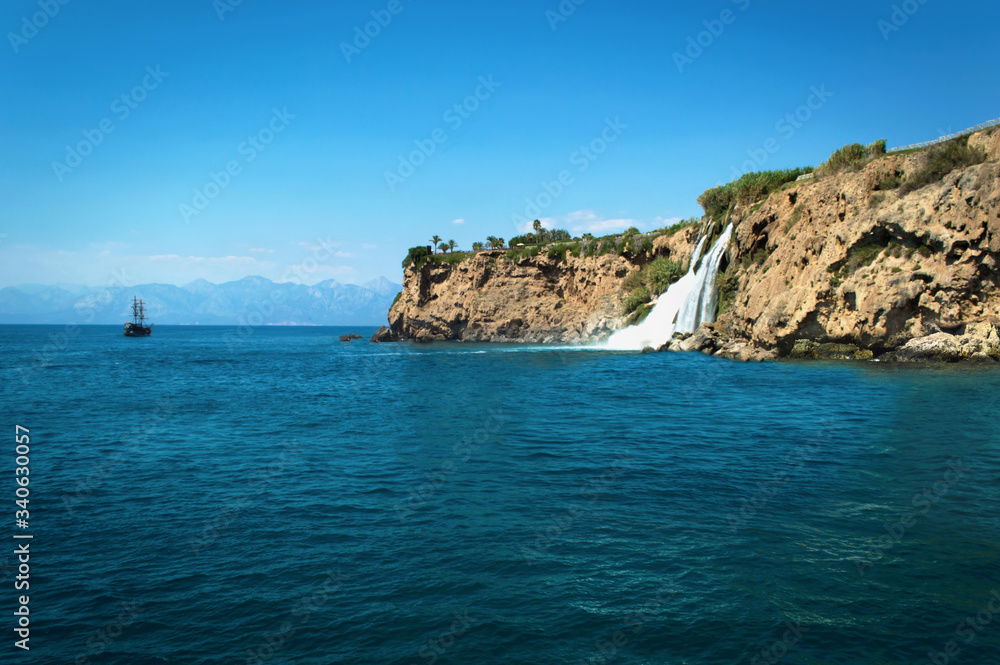 Landscape with a waterfall in the mountains. The medieval pirate ship in Turkey with tourists