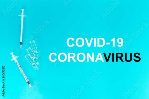 White words COVID-19 CORONAVIRUS. Syringe and ampoule on a blue background top view.