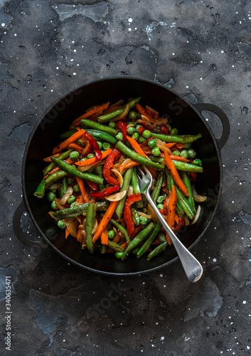 Green beans, sweet peppers, carrots, onions, green peas stir fry in a pan  on a dark background, top view. Fast diet vegetarian lunch, asian style