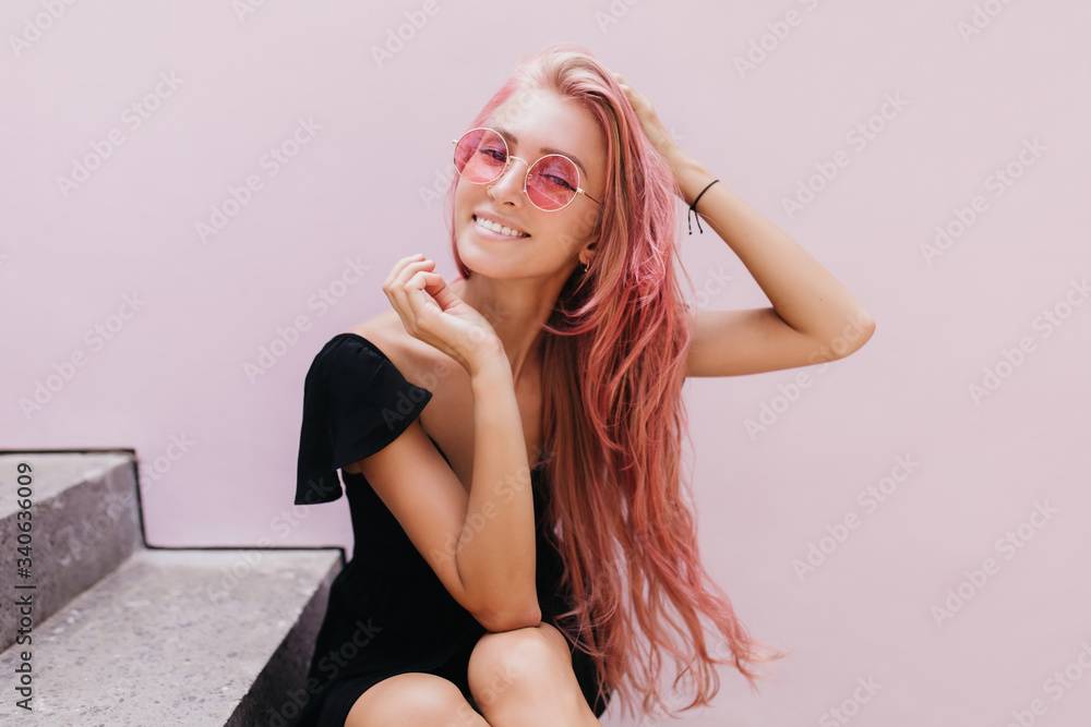 Amazing european woman chilling on stairs after walk around town and smiling to camera. Pink-haired inspired girl in dress posing on the steps. Amazing european woman chilling on stairs after walk around town and smiling to camera. Pink-haired inspired girl in dress posing on the steps.