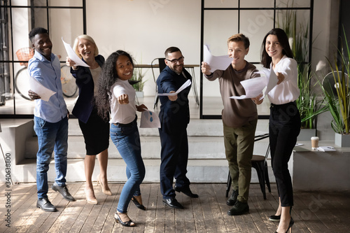 Overjoyed diverse multicultural employees have fun dancing with paperwork in office celebrating business victory together, happy multiethnic colleagues offer suggest good company service