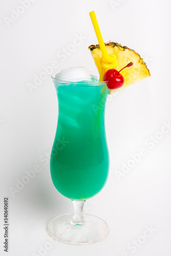 green alcohol cocktail top with coconut decorated with pineapple and red cherry in tall glass isolated on white