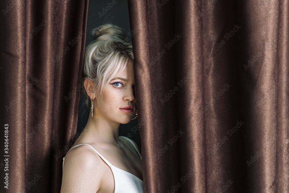 Obraz premium Sexy young blonde looking out from behind the curtains.