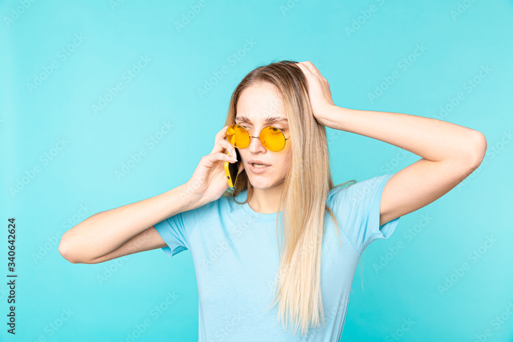 Young girl in trendy sunglasses talking on phone with surprised face expression. Indoor portrait of glamorous young woman holding smartphone and expressing perplexity.