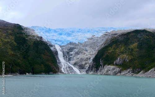 Glacier with waterfall in chilean fjord, blue ice and clouds, glacier alley, Beagle Channel