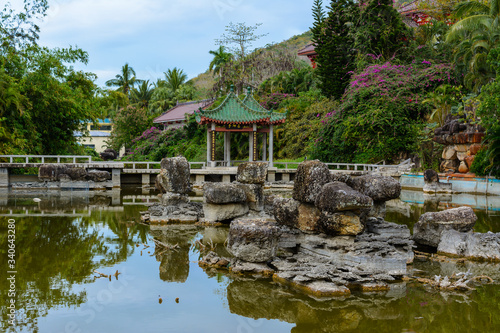 Green lake surrounded by gazebos, temples, mountains, flowers, palm grove and stone fence on the territory of Buddhist center Nanshan.