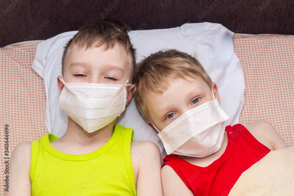 Two European brothers are lying on a bed in medical masks. Children got sick with the virus.