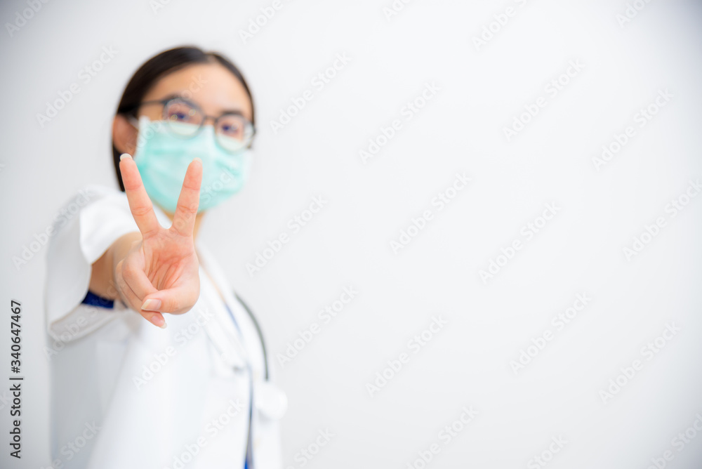 Studio portrait beautiful Asian young woman doctor raise two V shape finger wear a mask to safety Coronavirus to support in the fight against disease epidemic COVID 19 concept on blank gray background Studio portrait beautiful Asian young woman doctor raise two V shape finger wear a mask to safety Coronavirus to support in the fight against disease epidemic COVID 19 concept on blank gray background