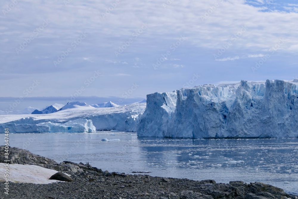 Glacier front with stone beach landscape in Antarctica, blue cloudy sky, Stonington Island Glacier front with stone beach landscape in Antarctica, blue cloudy sky, Stonington Island