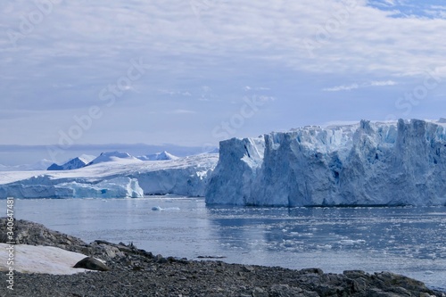 Glacier front with stone beach landscape in Antarctica, blue cloudy sky, Stonington Island