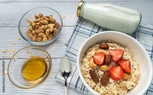 Fototapeta Naklejka Na Ścianę i Meble -  Bowls of oatmeal with almond milk, nuts, honey and fruits on white wood background.  Healthy Homemade concept. vegan food