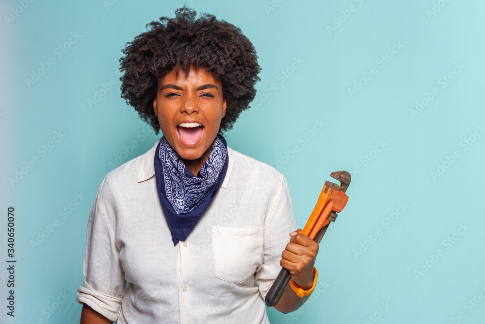 Black young woman with black power hair screaming using a stillson key Black young woman with black power hair screaming using a stillson key