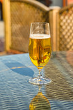 Glass of golden beer lager on the glass table top of garden furniture