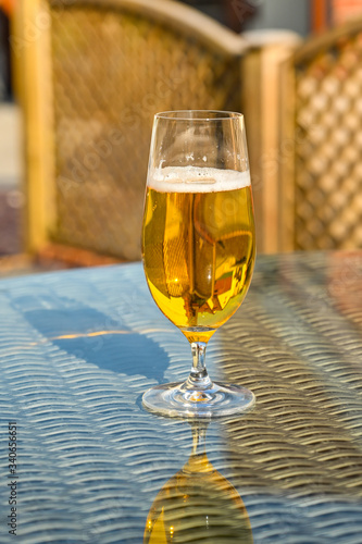 Glass of golden beer lager on the glass table top of garden furniture
