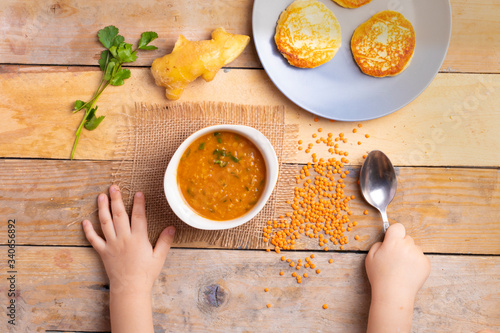 Delicious lentil cream-soup with pancake, top view and kids hands