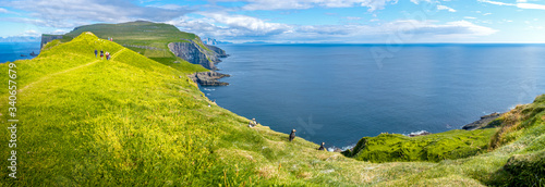 Panoramic view over mythical Faroe Island Mykines in the middle of Atlantic Ocean with a lot of puffins, parrot like seabirds, and hikers, summer, blue sky © neurobite