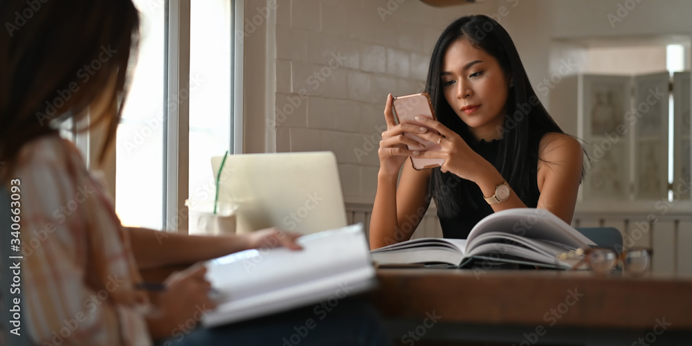 Beautiful women reading a book and relaxing together while sitting at the wooden table over comfortable sitting room as background. Women with relaxing time concept. Beautiful women reading a book and relaxing together while sitting at the wooden table over comfortable sitting room as background. Women with relaxing time concept.