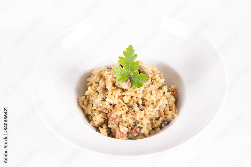 Risotto with button mushroom and bacon decorated with parsley on a plate on a white background
