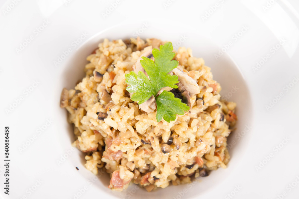 Risotto with button mushroom and bacon decorated with parsley on a plate on a white background Risotto with button mushroom and bacon decorated with parsley on a plate on a white background