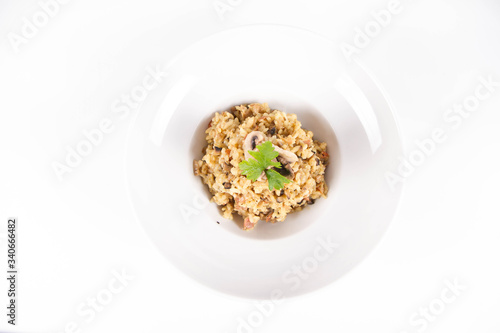 Risotto with button mushroom and bacon decorated with parsley on a plate on a white background