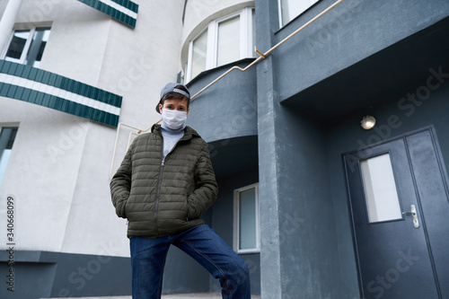 teen boy posing near wall of high-rise buildings with apartments, a residential area, a medical mask on his face protects against viruses and dust