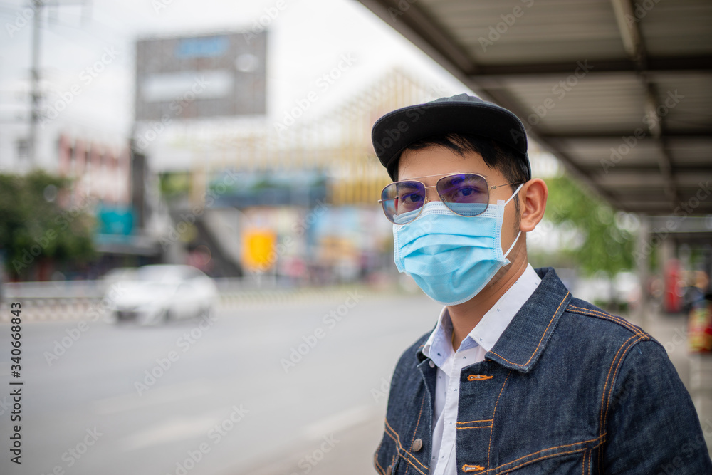 Asian Young man standing in the city and wearing protection mask on face for protection air pollution, particulates and for protection flu virus, influenza, coronavirus at city Asian Young man standing in the city and wearing protection mask on face for protection air pollution, particulates and for protection flu virus, influenza, coronavirus at city