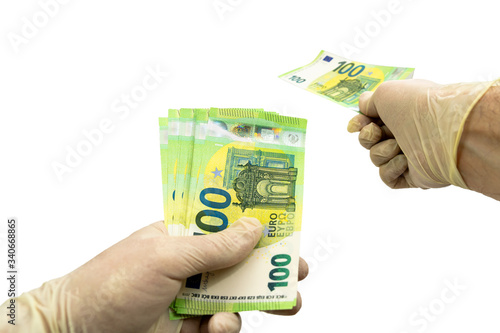 Two hands in white protective gloves hold a bundle of 100 Euro bills. Isolated white background. Virus protection concept. The second hand holds out euro money while paying for the purchase.