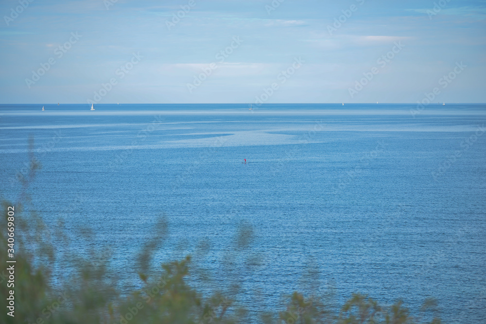 Lonely surfer in the Mediterranean Sea, against the backdrop of yachts and the horizon.