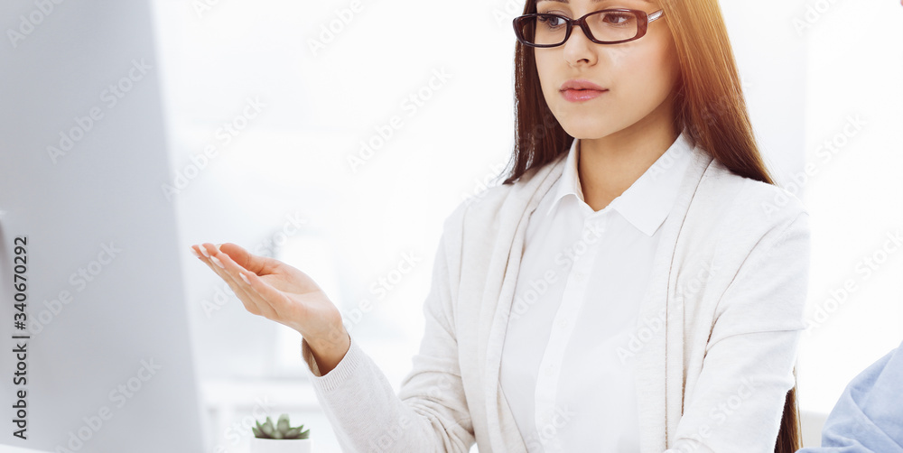 Beautiful young woman sitting at the desk with computer in sunny office. Looks like student girl or business lady communicating with casual dressed man Beautiful young woman sitting at the desk with computer in sunny office. Looks like student girl or business lady communicating with casual dressed man