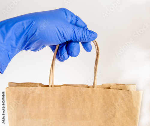 A hand in a rubber glove holds a paper shopping bag, food delivery in eco-friendly packaging, zero waste photo