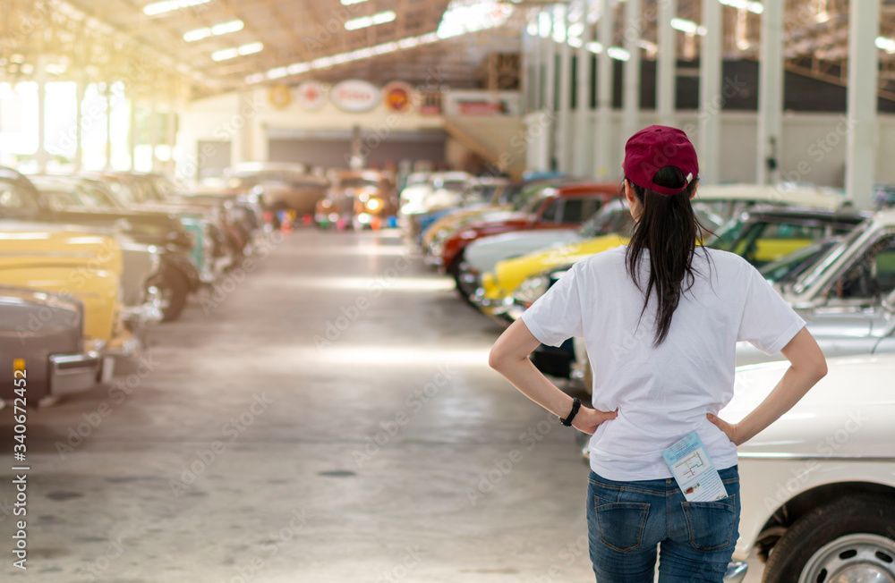Young women standing in car garage looking at old vintage car. Women is a vintage car showroom looking for a car. Young women standing in car garage looking at old vintage car. Women is a vintage car showroom looking for a car.