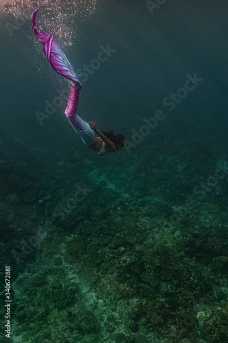 Young female free diver swims underwater in a colorful and sexy mermaid costume.