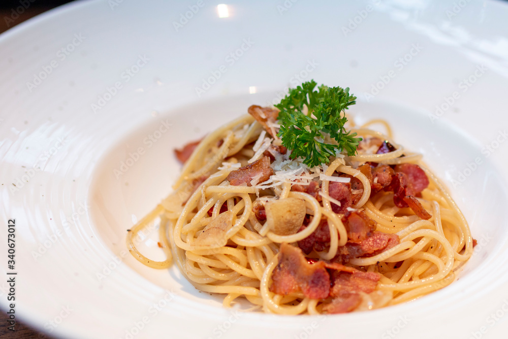 Spaghetti with bacon in white plate for eating concept. Spicy spaghetti with bacon and basil. Spaghetti with pork sausage and tomato sauce on white plate.