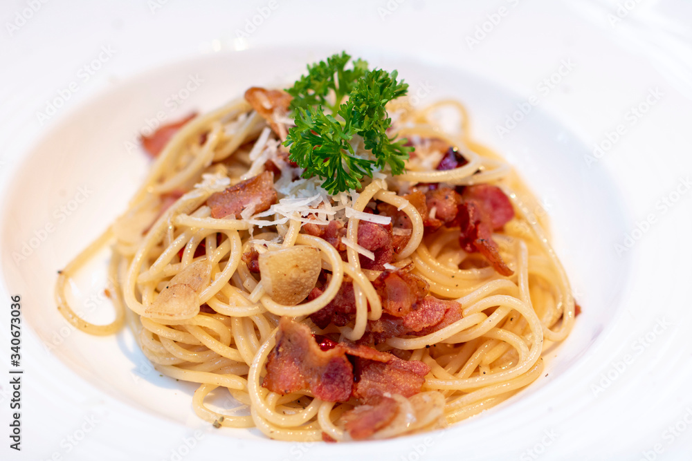 Spaghetti with bacon in white plate for eating concept. Spicy spaghetti with bacon and basil. Spaghetti with pork sausage and tomato sauce on white plate.