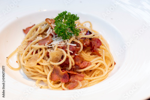Spaghetti with bacon in white plate for eating concept. Spicy spaghetti with bacon and basil. Spaghetti with pork sausage and tomato sauce on white plate.
