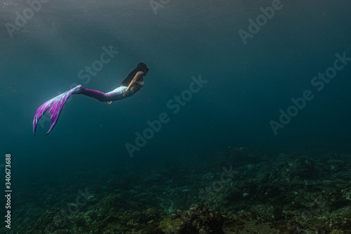 Young female free diver swims underwater in a colorful and sexy mermaid costume. photo