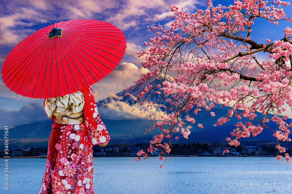 Asian women wear Japanese kimonos. Holding a red umbrella at Mount Fuji and cherry blossoms at