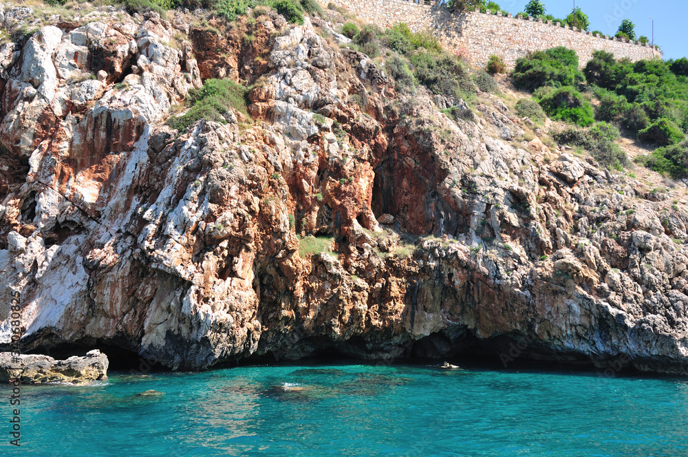Fototapeta premium Rocky and cliff shore over the sea. Turquoise-coloured seawater.