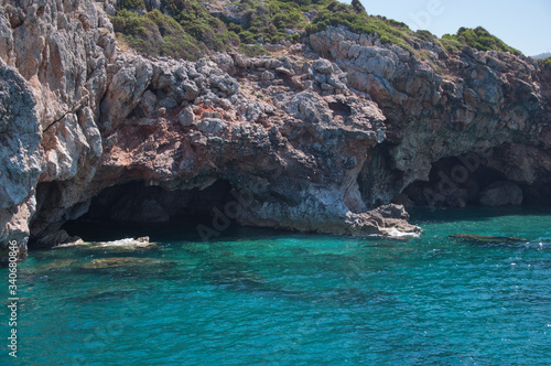 Rocks rise above the transparent turquoise sea. The rocks have an entrance to the caves.