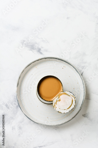 Condensed or evaporated milk in open tin on light concrete table. Top view.