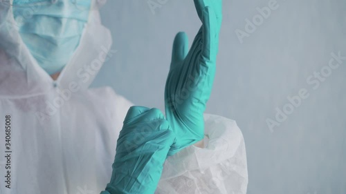 Coronavirus pandemic. A young nurse wearing a protective suit puts on gloves before starting work. Close-up. photo
