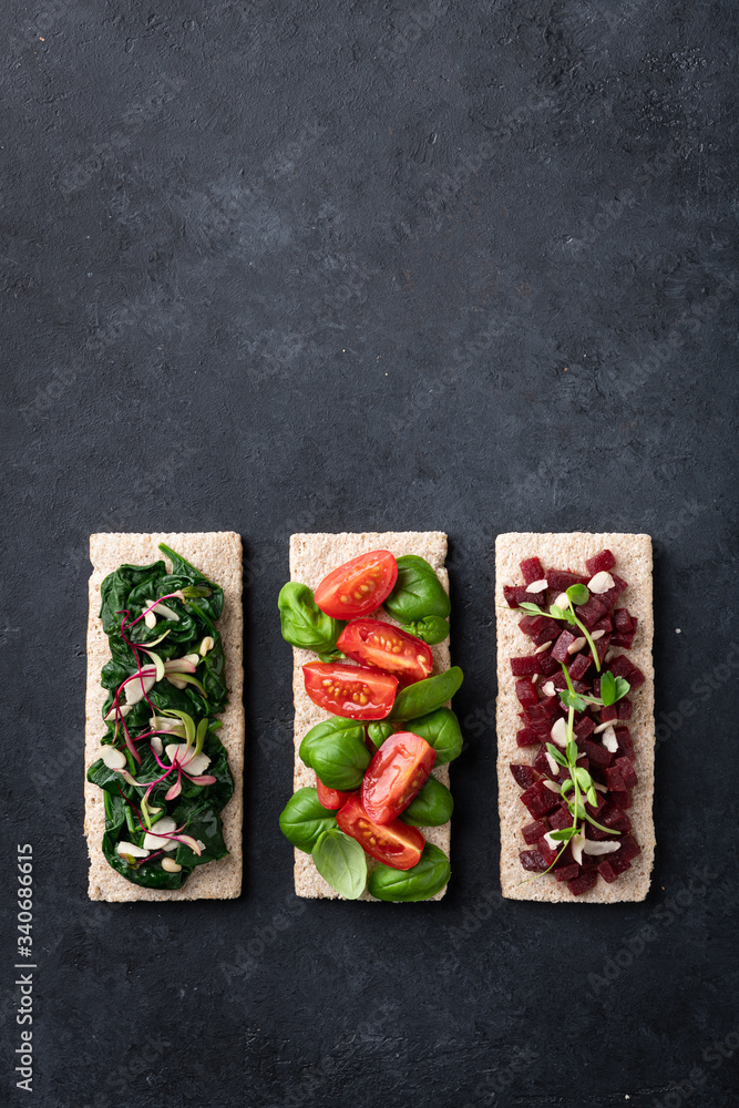 Fototapeta premium vegan sandwiches with spinach, nuts, tomatoes, basil, beets and micro greens on a black background. View from above.