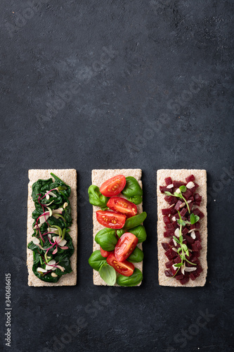 vegan sandwiches with spinach, nuts, tomatoes, basil, beets and micro greens on a black background. View from above.