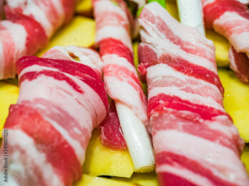 Raw spring onion with rolled bacon. Typical Sicilian street dish called 'Cipollata' roasted on the grill and roasted potatoes as a side dish. photo