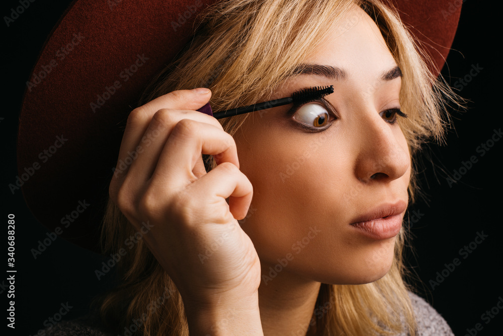 Portrait of accurate concentrated young blonde woman using mascara for eyelashes. Making volume. Isolated over pink background.